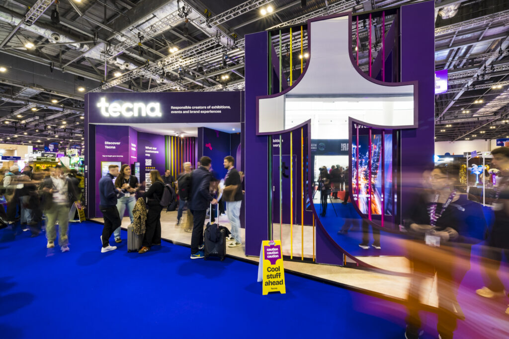 Tecna's purple exhibition stand design with bold overhead structure and open sightlines, drawing visitor attention from the aisle at a busy trade show