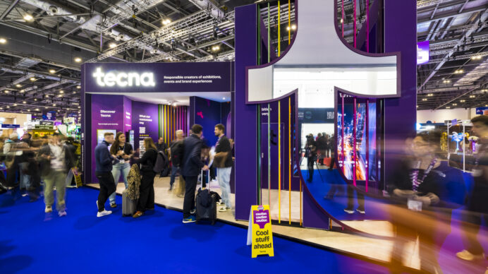 Tecna's purple exhibition stand design with bold overhead structure and open sightlines, drawing visitor attention from the aisle at a busy trade show