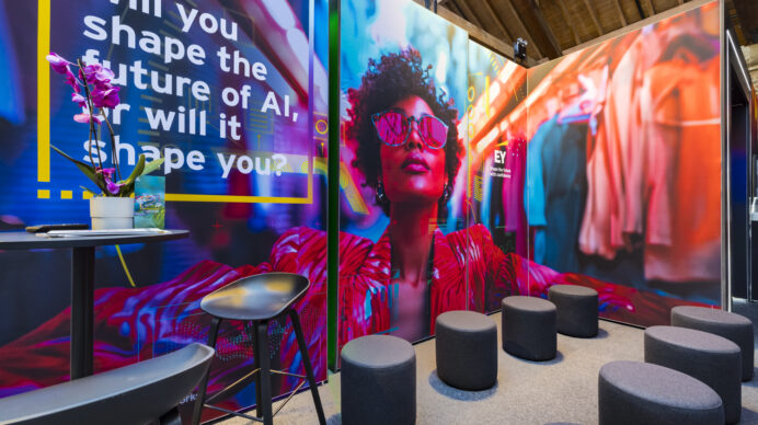 Colourful branded exhibition stand featuring a striking digital display, ambient lighting, and lounge-style seating designed to encourage visitors to dwell.