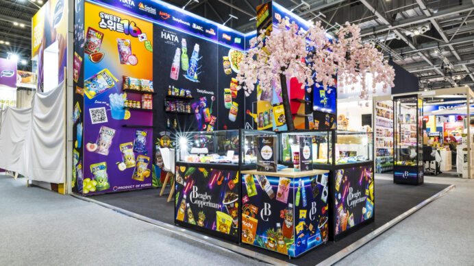 Vibrant confectionery exhibition stand with branded shopfront displays and a cherry blossom centrepiece, showcasing detailed product-focused stand design at a first-time show.