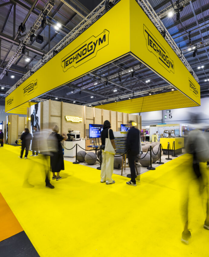 Bold yellow exhibition stand design with suspended branded signage, illustrating how standout exhibition stands attracts visitor attention at UK trade shows