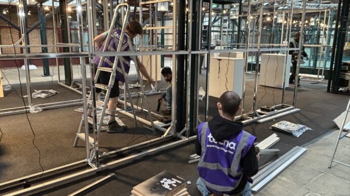 A team of exhibition stand builders building a modular frame during trade show build-up, illustrating the fabrication process behind a finished stand