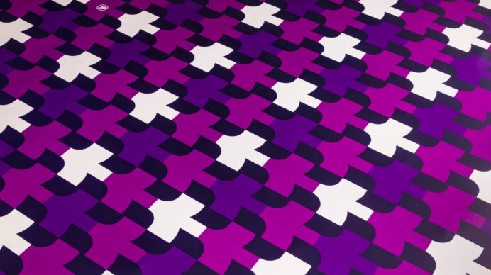 Close-up of a purple, magenta, and white geometric patterned carpet with an abstract interlocking cross design