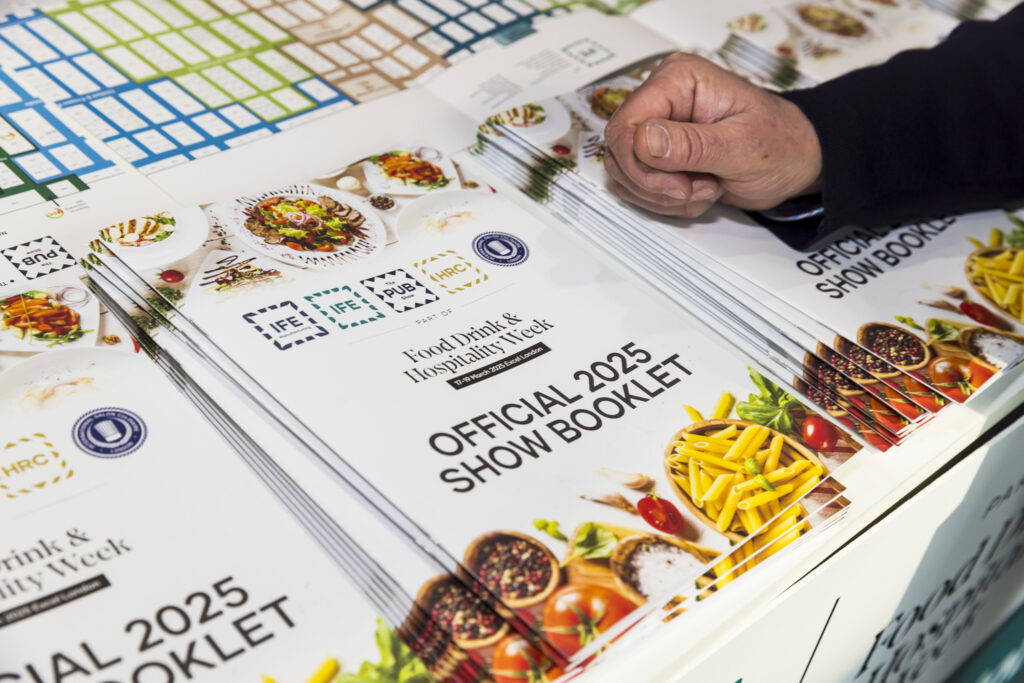 Attendee picking up an official show booklet from a stack at a trade show