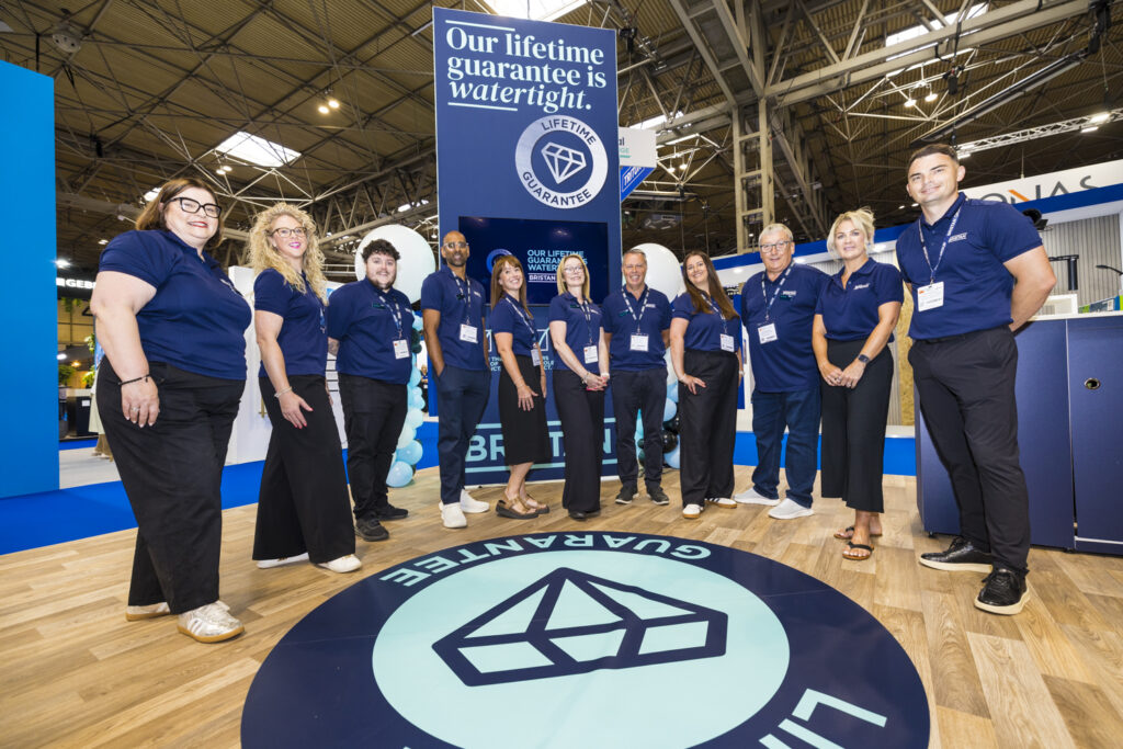 Full exhibition stand team in matching navy polo shirts lined up and smiling in front of a 'Lifetime Guarantee' branded booth