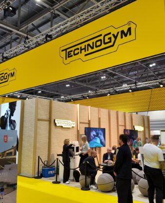 Technogym exhibition stand with bold yellow branding and overhead signage on a busy trade show floor.